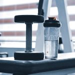 Close-up of dumbbell and water bottle on a gym bench, emphasizing fitness routine.