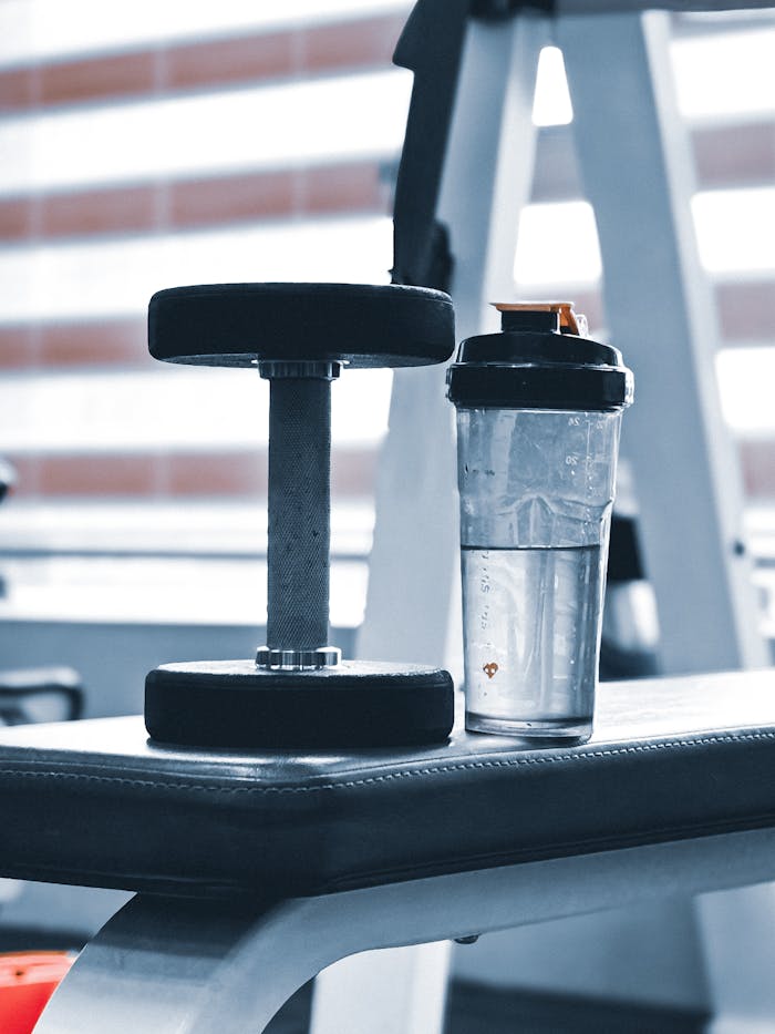 Close-up of dumbbell and water bottle on a gym bench, emphasizing fitness routine.